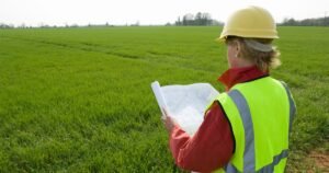 Insights 73 A surveyor in a hi-vis vest and hard hat holding plans in a green field — environmental searches for UK property