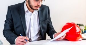 Insights 64 Engineer in a suit reviewing construction plans with a red hard hat on the desk — JCT contracts in the UK