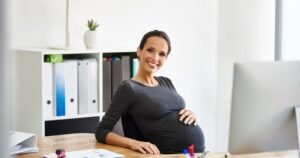 Insights 58 Smiling pregnant businesswoman working at her desk in a UK office — maternity and family leave