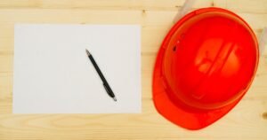 Insights 63 Orange hard hat beside a blank document and pen on a wooden surface — NEC construction contracts in the UK