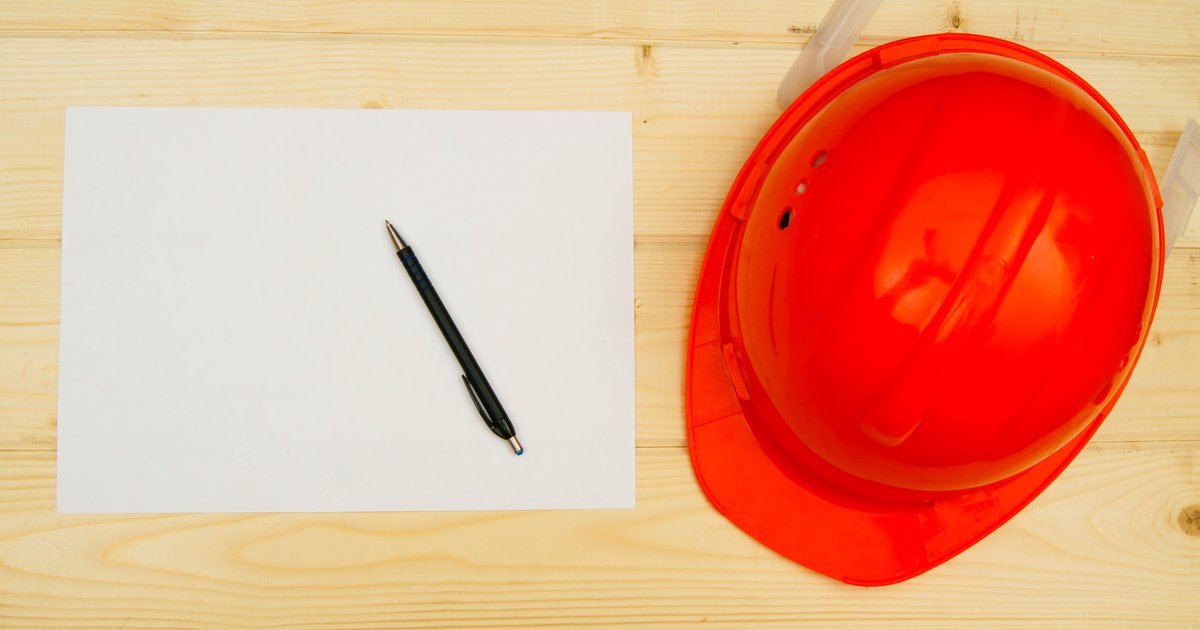 Orange hard hat beside a blank document and pen on a wooden surface — NEC construction contracts in the UK
