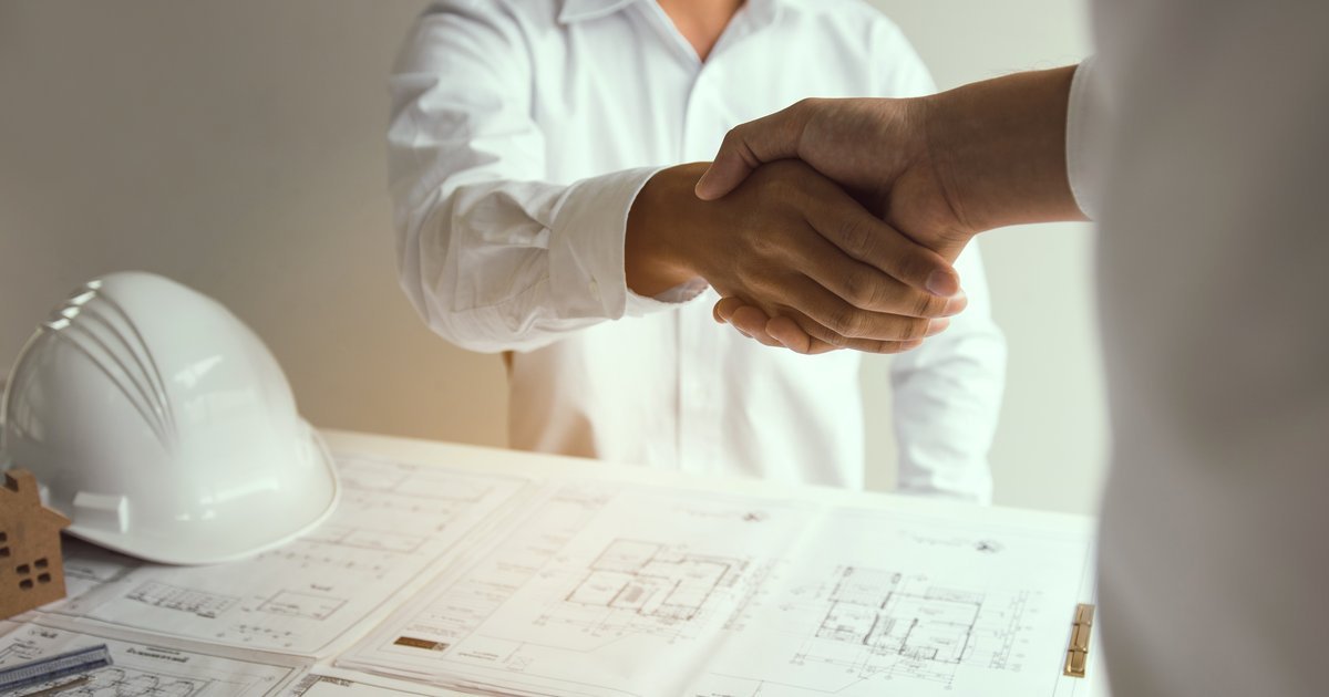 Professionals shaking hands over engineering blueprints and a hard hat — performance bonds in UK construction