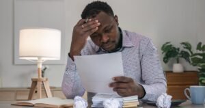 Insights 62 Frustrated man holding his head while reading a letter with crumpled papers on a desk — challenging a rejected insurance claim in the UK