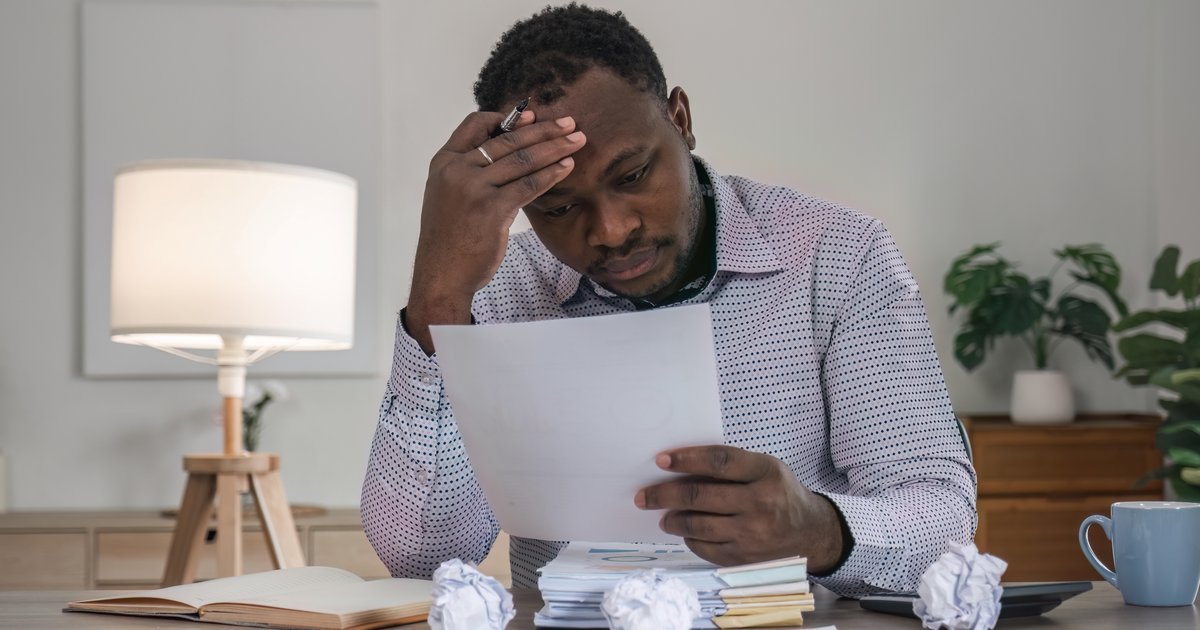 Frustrated man holding his head while reading a letter with crumpled papers on a desk — challenging a rejected insurance claim in the UK