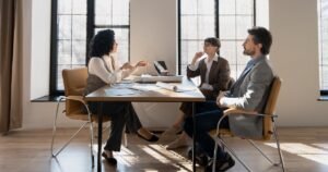 Insights 57 Three colleagues seated around a table in a bright office having a calm discussion — workplace mediation in the UK