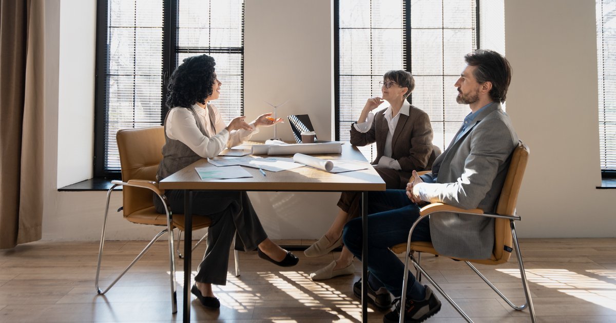 Three colleagues seated around a table in a bright office having a calm discussion — workplace mediation in the UK